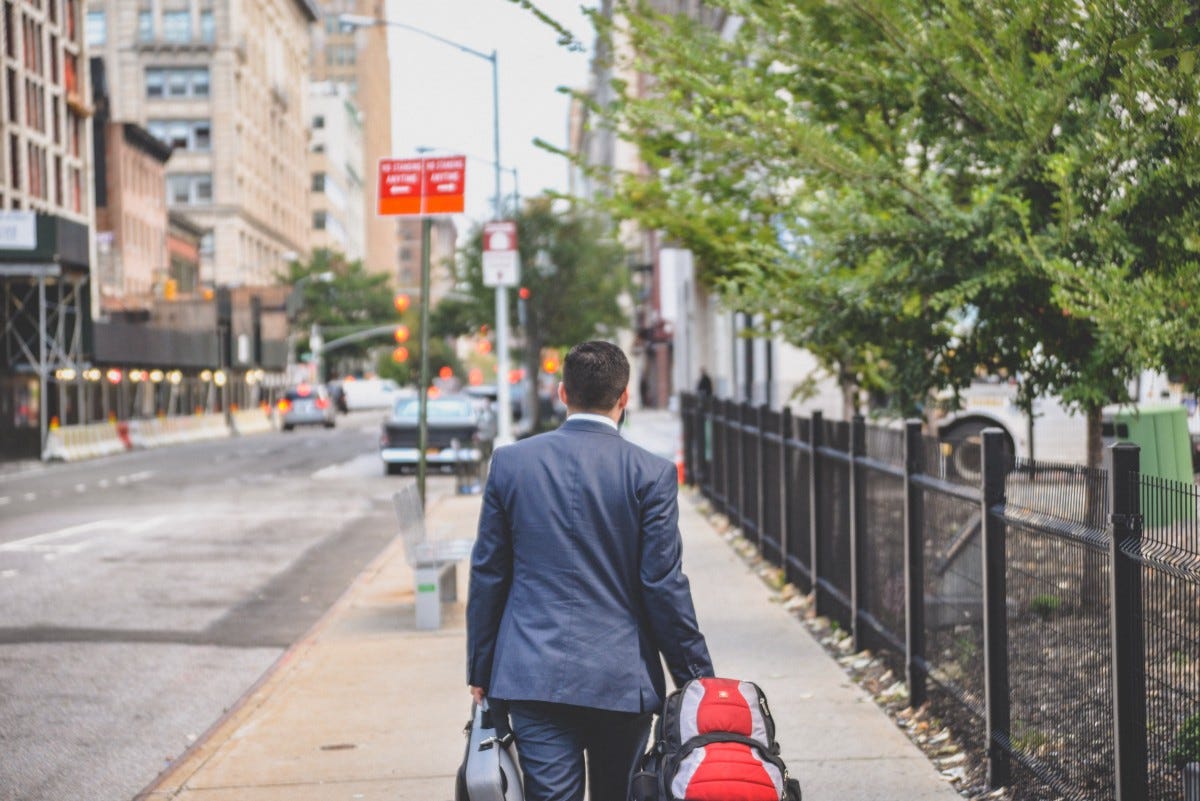 person in black suit jacket with r ed bag walking beside metal fence person in black suit jacket with r ed bag walking beside metal fence