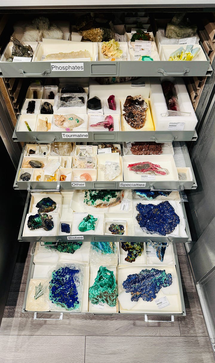 Open specimen drawers in the mineral research collection at the Natural History Museum of Los Angeles County, showing rows of labeled minerals including beryl, corundum, spodumene, opals, quartz, and feldspar, each specimen boxed and catalogued.