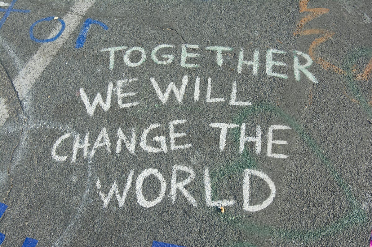 Together we will change the world written in white chalk on gray concrete