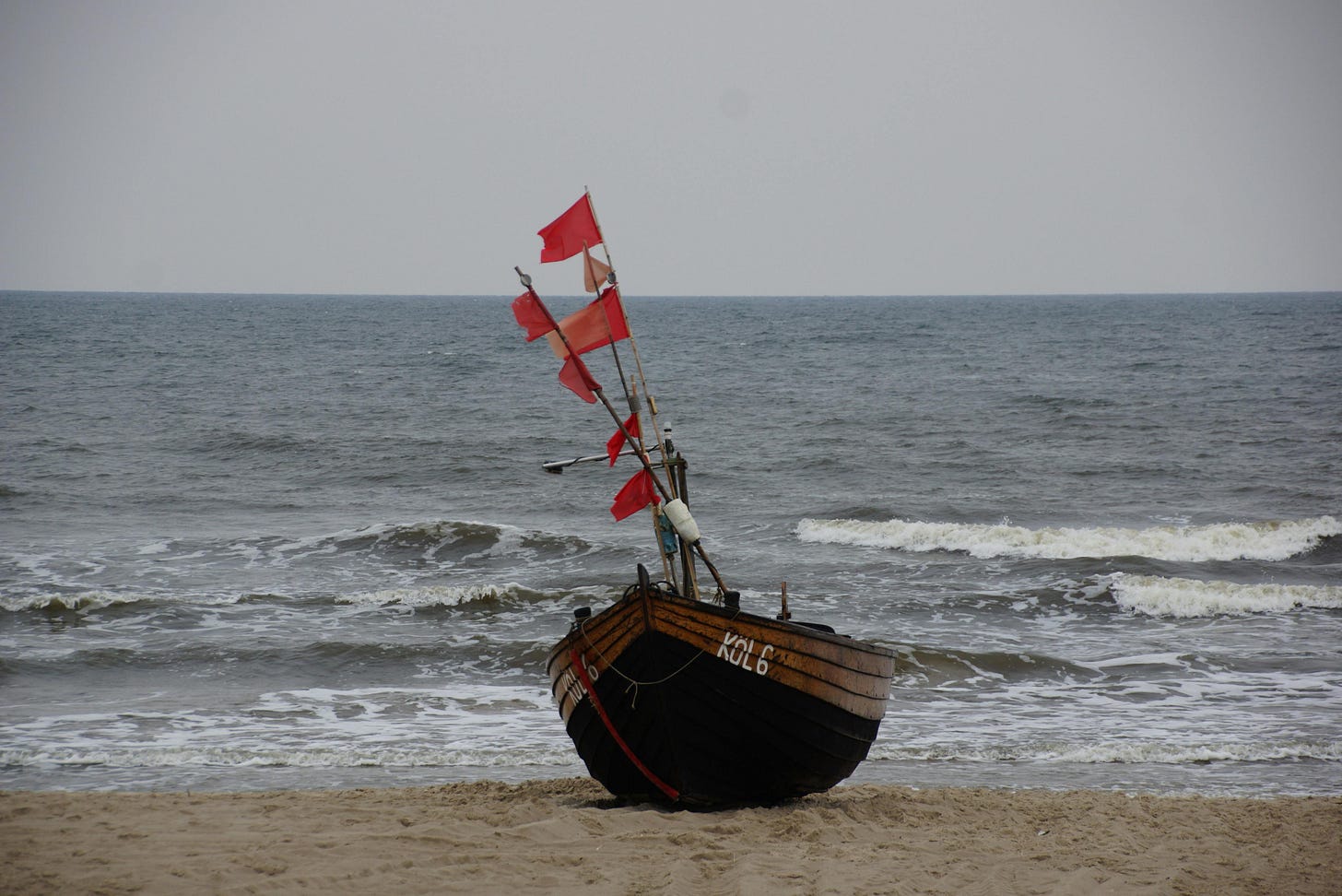old boat beached on sand waving red distress flags old boat beached on sand waving red distress flags