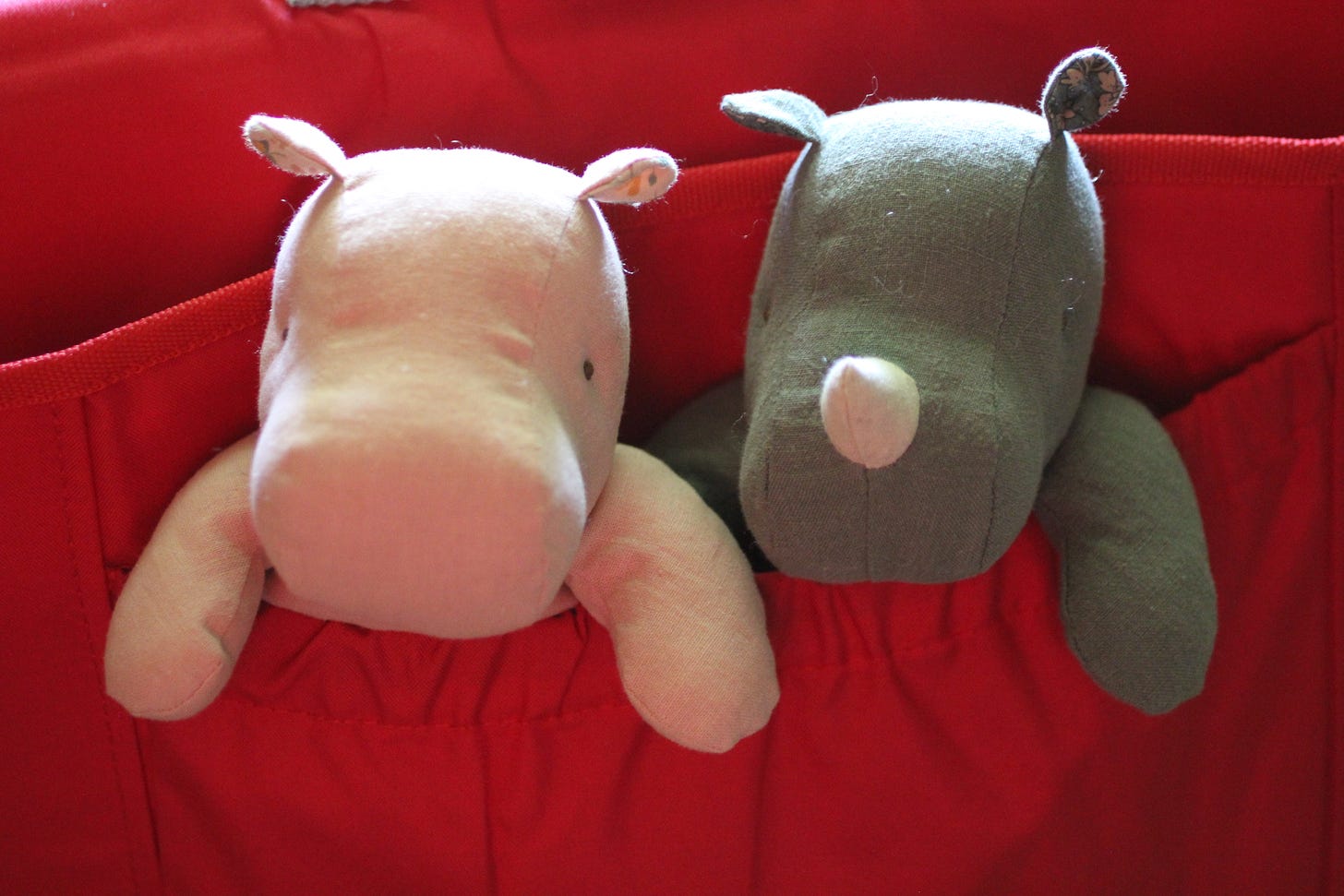 Soft pink and gray plush toys, Topsy and Pilly, sitting side by side in a bright red fabric pocket.