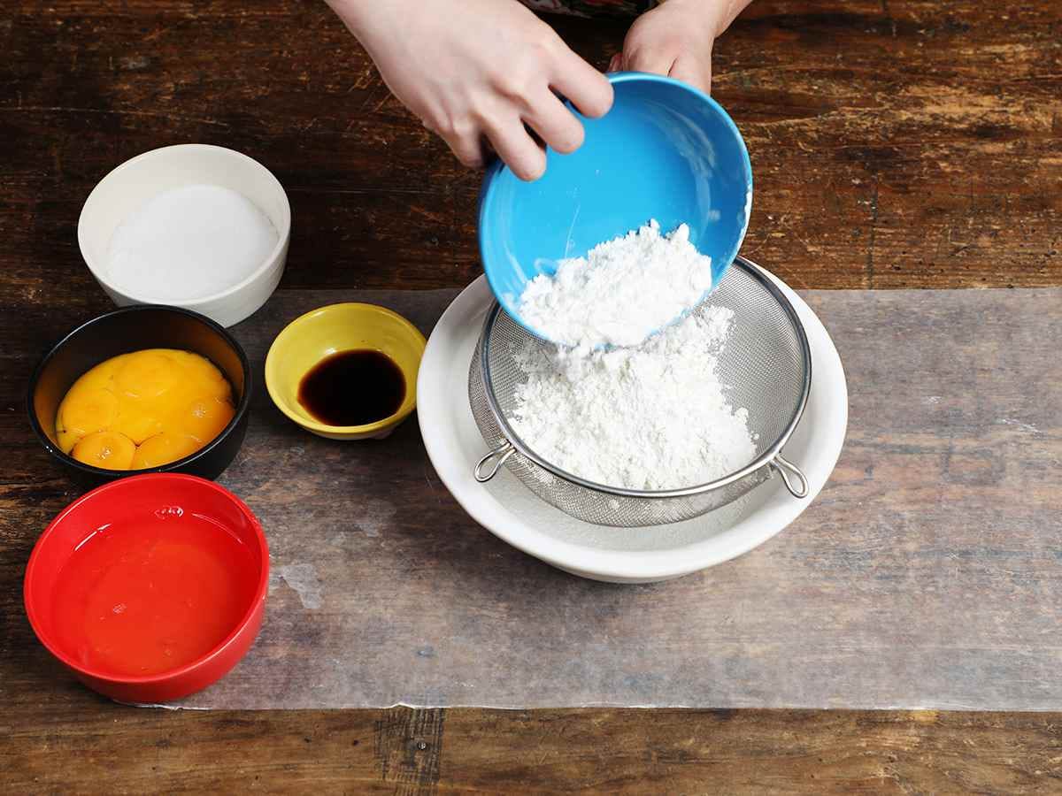 Pouring flour from blue bowl into mesh strainer