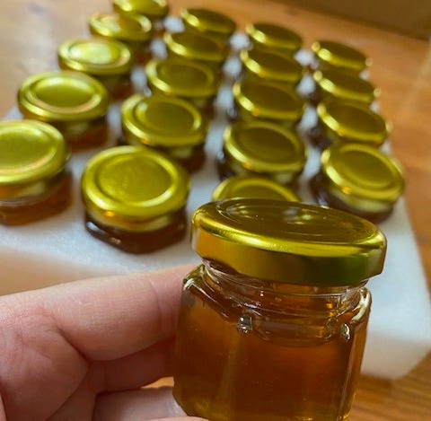 a hand holding a small jar of honey next to a tray of jars