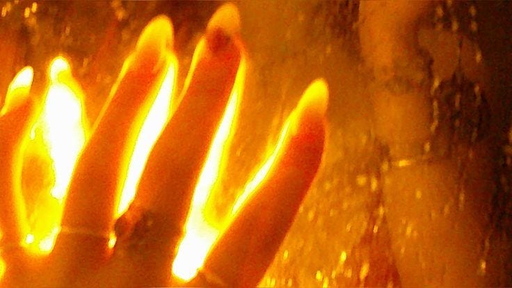 This may contain: a person's hand is shown through a window with yellow light coming from it