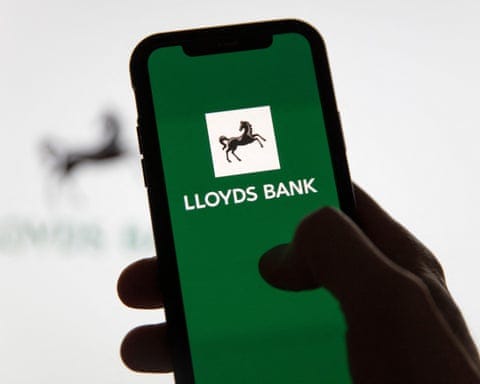 A hand holds a smartphone displaying the Lloyds Bank logo on a green screen A hand holds a smartphone displaying the Lloyds Bank logo on a green screen
