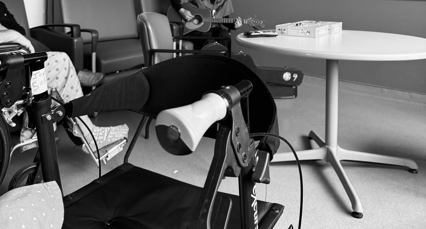 Patients in a hospital listening to a man singing and playing guitar.