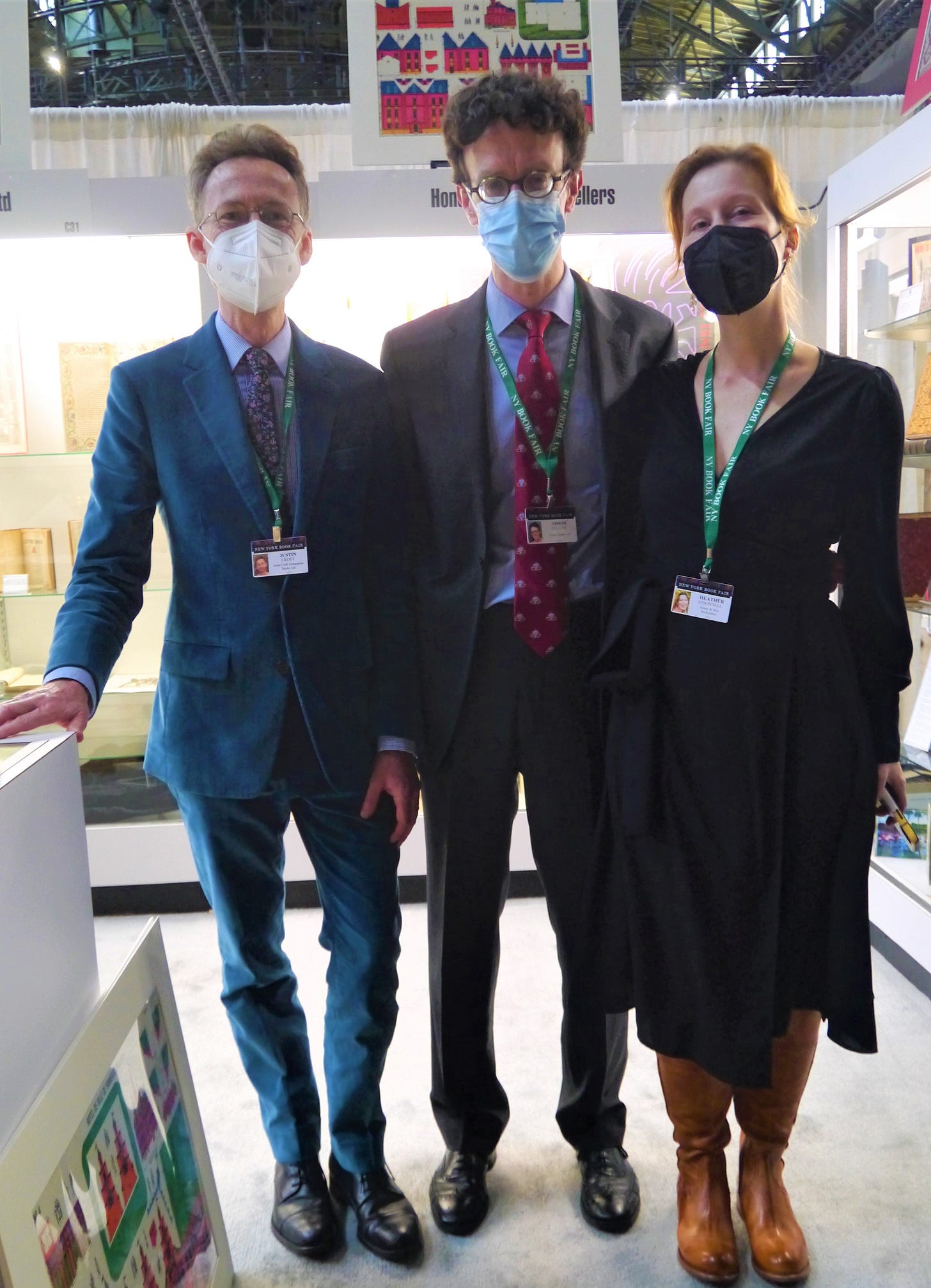 Justin Croft stands on the left in blue suit, Simon Beattie in the center in grey suit, and Heather O'Donnell on the right in a black dress all in front of their book stall