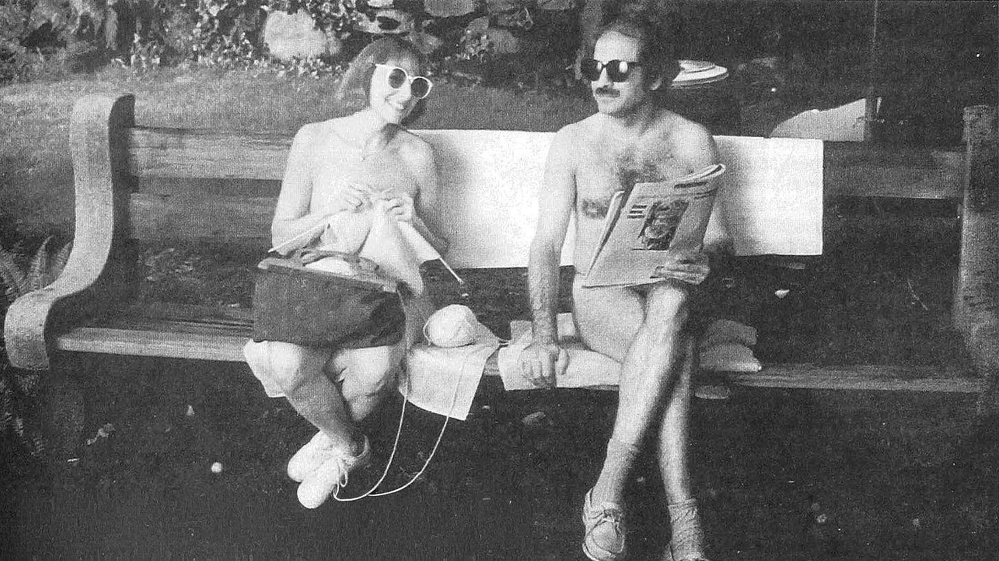Black-and-white photograph of Helene Williams and Leonard Lehrman, nude and wearing sunglasses, seated on a park bench during a commercial shoot. Helene knits while Leonard reads a newspaper.