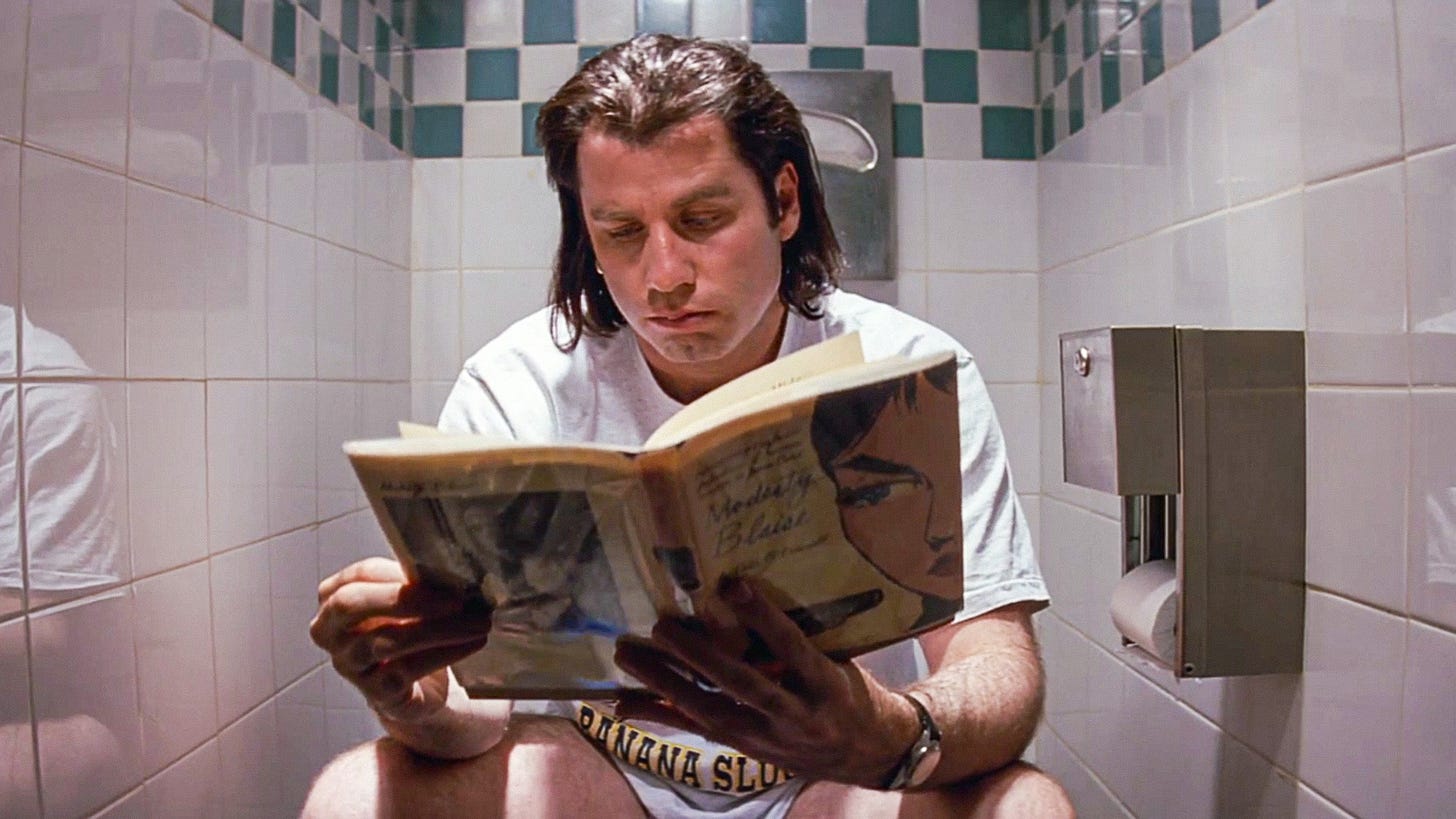 John Travolta sitting on toilet reading.