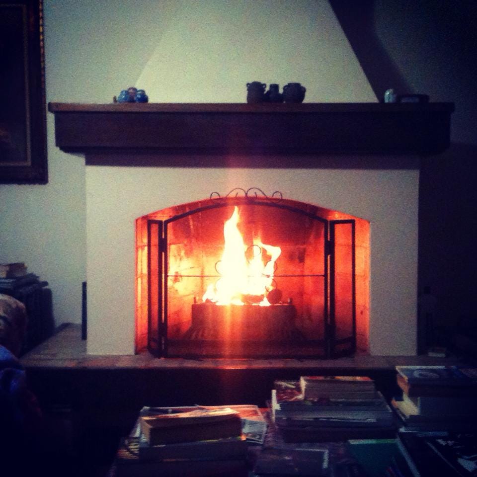 A lit fireplace in a darkened room, with a coffee table in front of it and some books piled up. A lit fireplace in a darkened room, with a coffee table in front of it and some books piled up.
