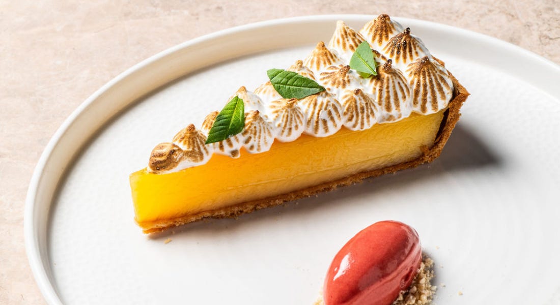 A lemon tart with meringue on top and red sorbet next to it, on top of a white plate