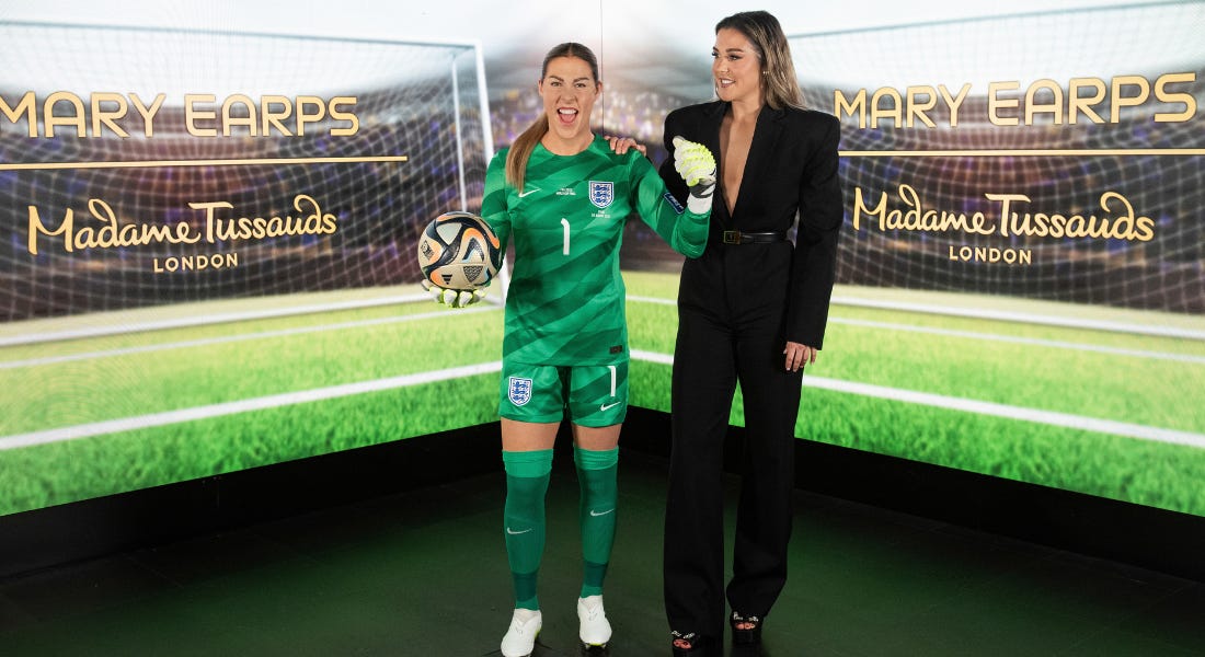 A Mary Earps waxwork wearing a green goalkeeper kit holding a football, next to the real Mary Earps wearing a black suit, with a goalpost background behind them A Mary Earps waxwork wearing a green goalkeeper kit holding a football, next to the real Mary Earps wearing a black suit, with a goalpost background behind them
