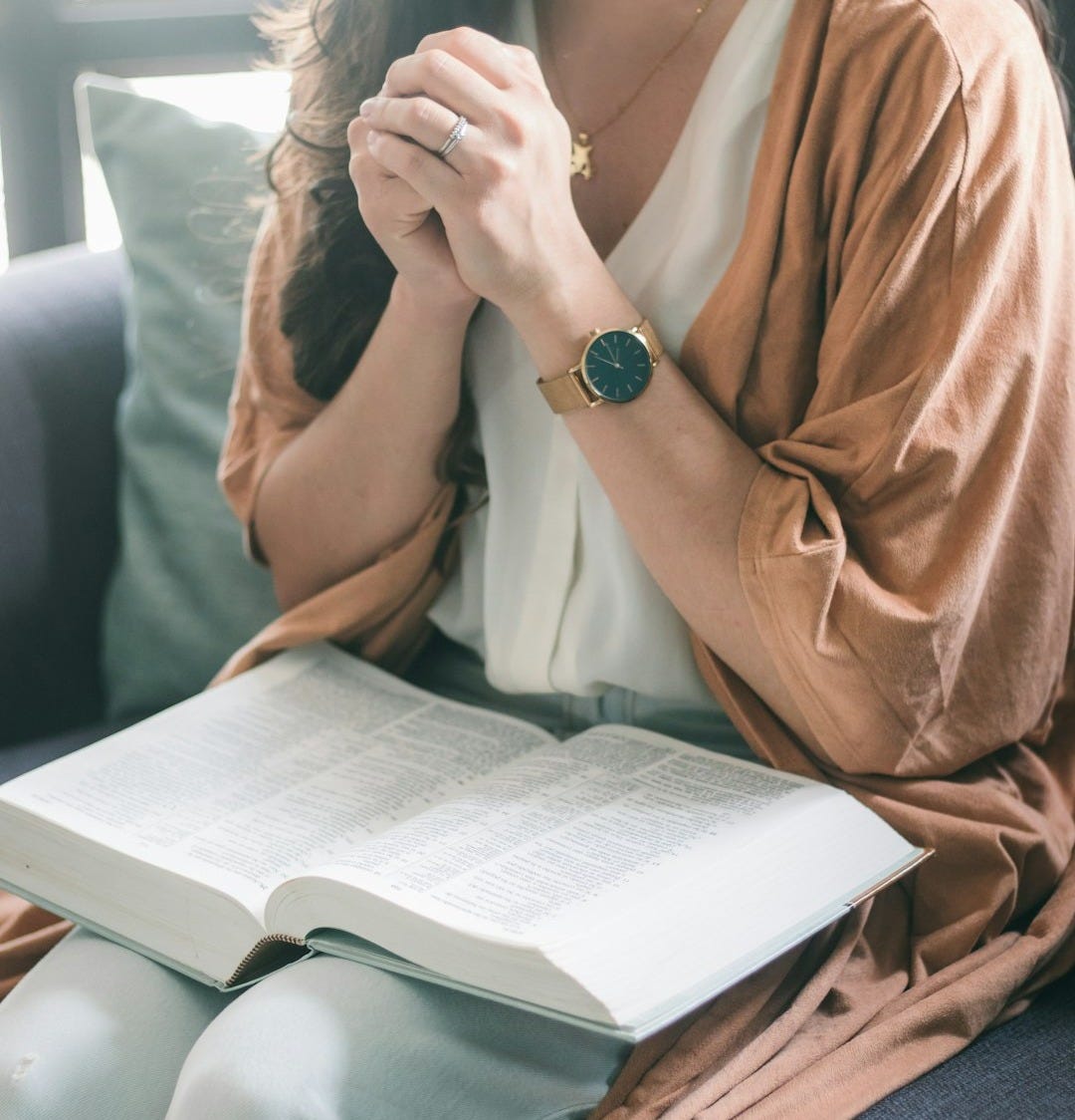 girl sitting with hands clasped and open Bible on her lap girl sitting with hands clasped and open Bible on her lap
