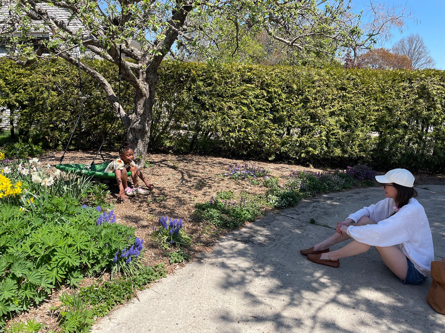 a white mom sits on the ground talking to her Black kid