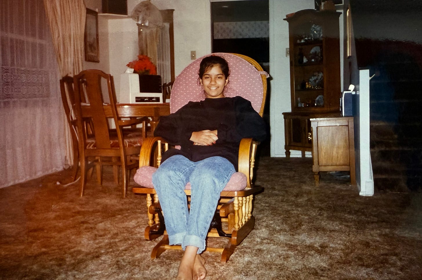 young woman sitting on cushioned wooden chair smiling atop brown carpet in what appears to be a living room