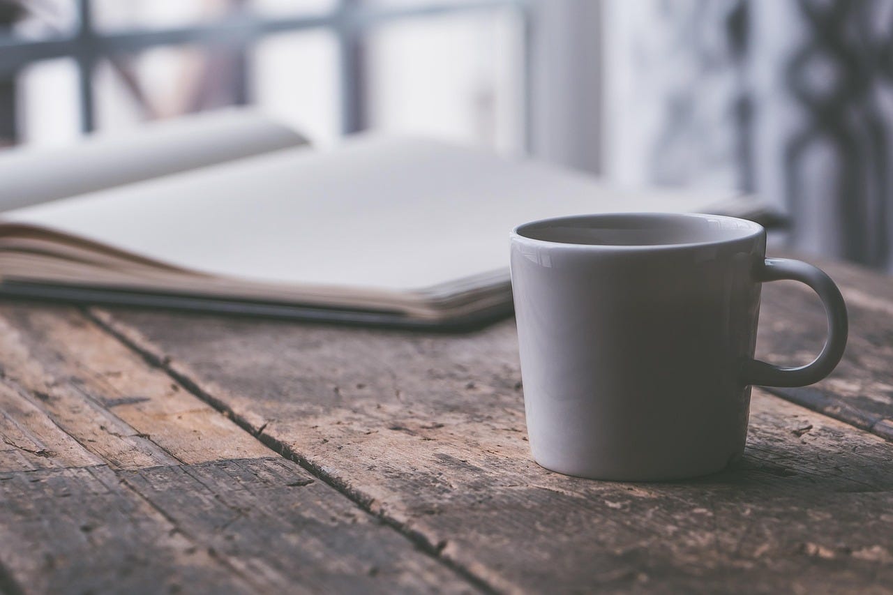 White ceramic mug on a rustic wooden table beside an open journal in soft morning light. White ceramic mug on a rustic wooden table beside an open journal in soft morning light.