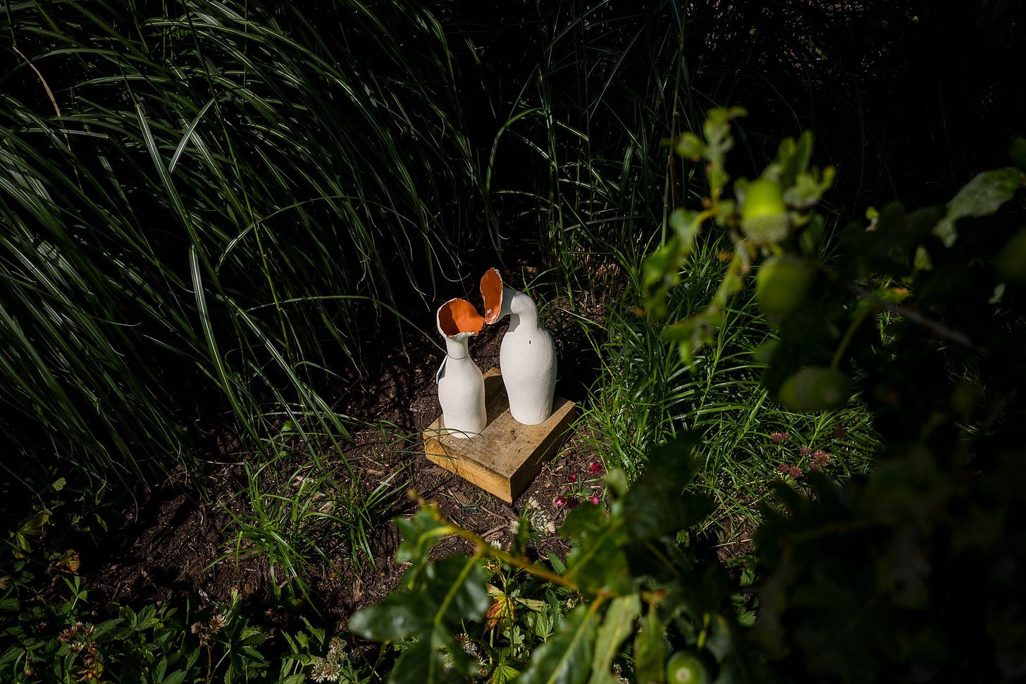Small pottery works painted white and orange act like flowers in the grass.