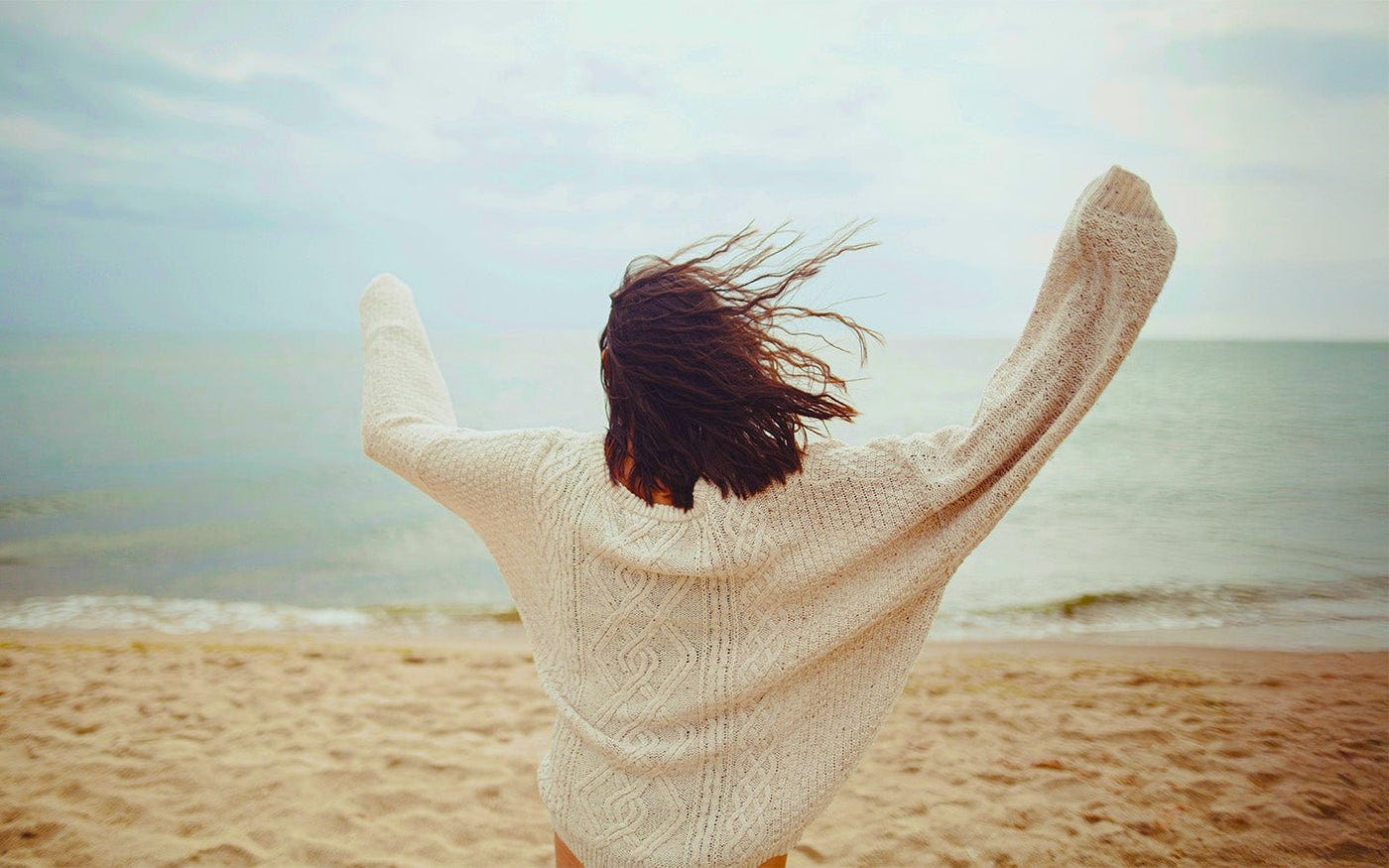 Woman with arms raised looking at the ocean