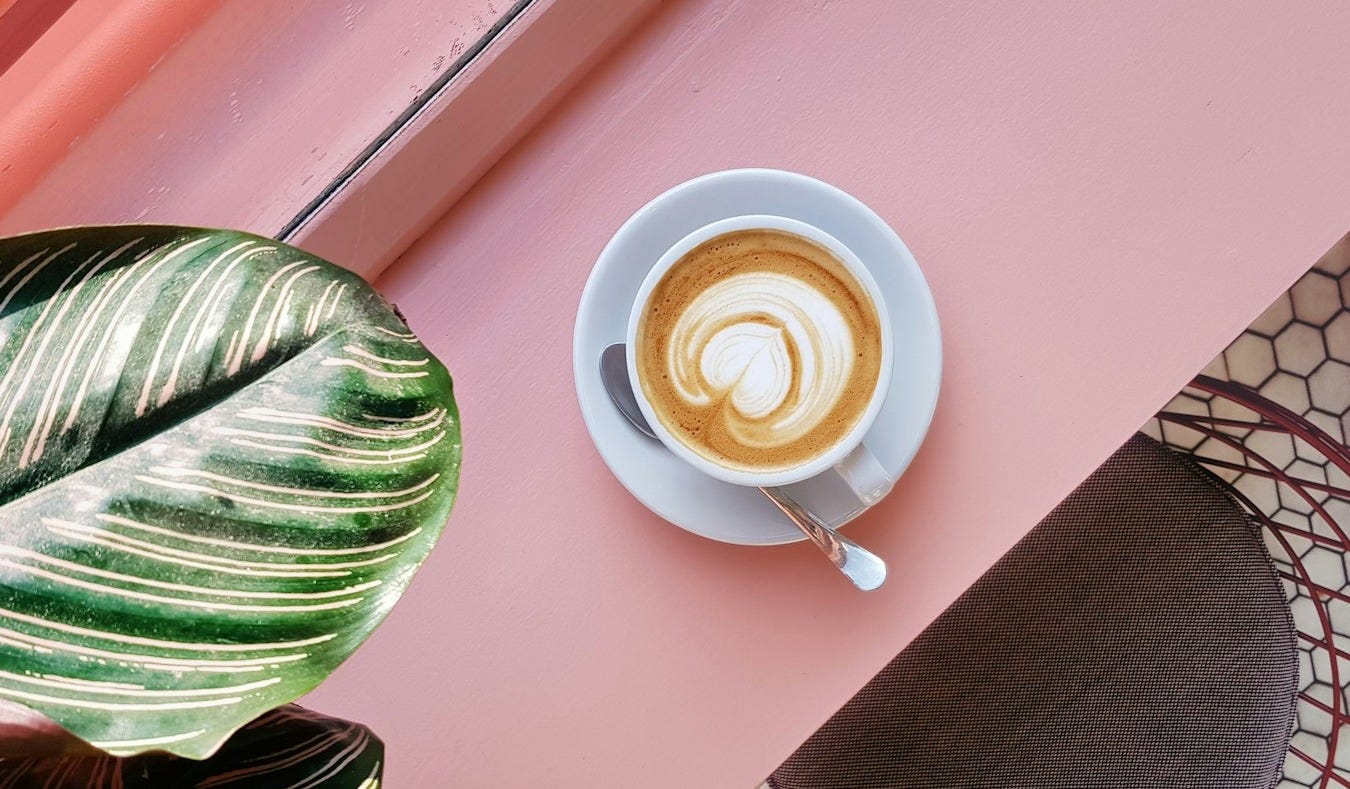 cup of coffee on saucer with teaspoon on pink tabletop