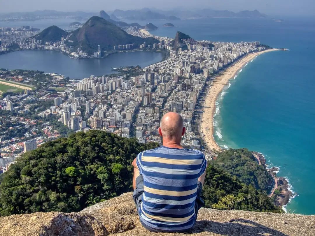 Ian sitting at the summit looking out towards buildings, beach and sea