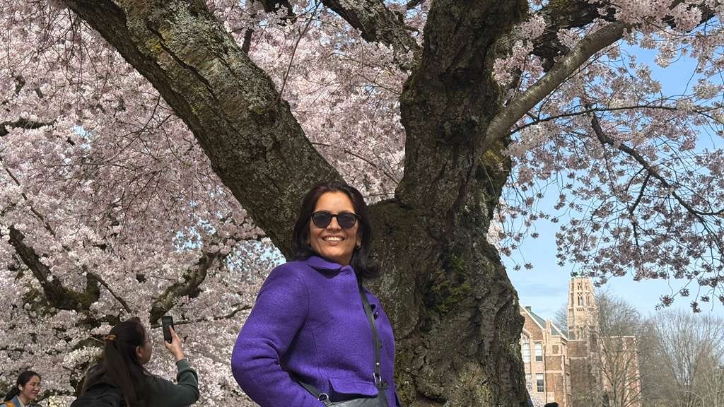 Anu Arora smiles in front of a cherry blossom tree on the University of Washington quad