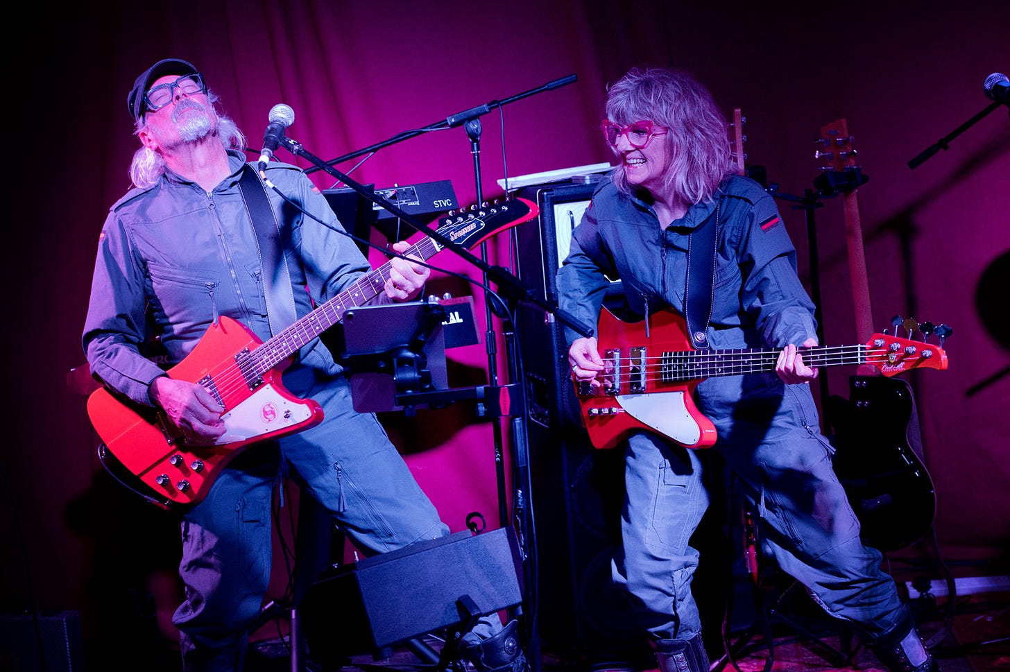A man playing a red guitar on the left and a woman playing a red bass guitar on the right - Starlite & Campbell concert