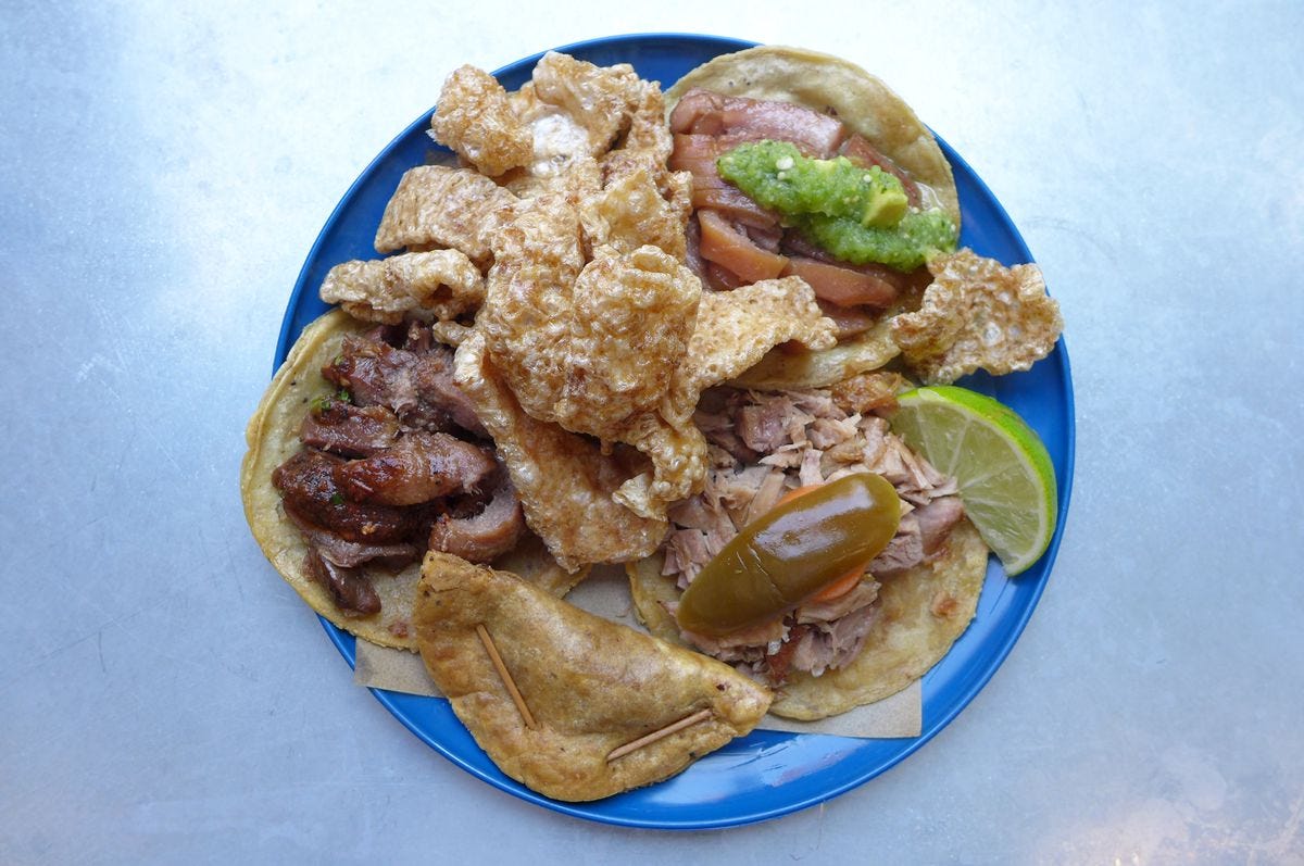 Four tacos on a blue plate with fried pig skin.