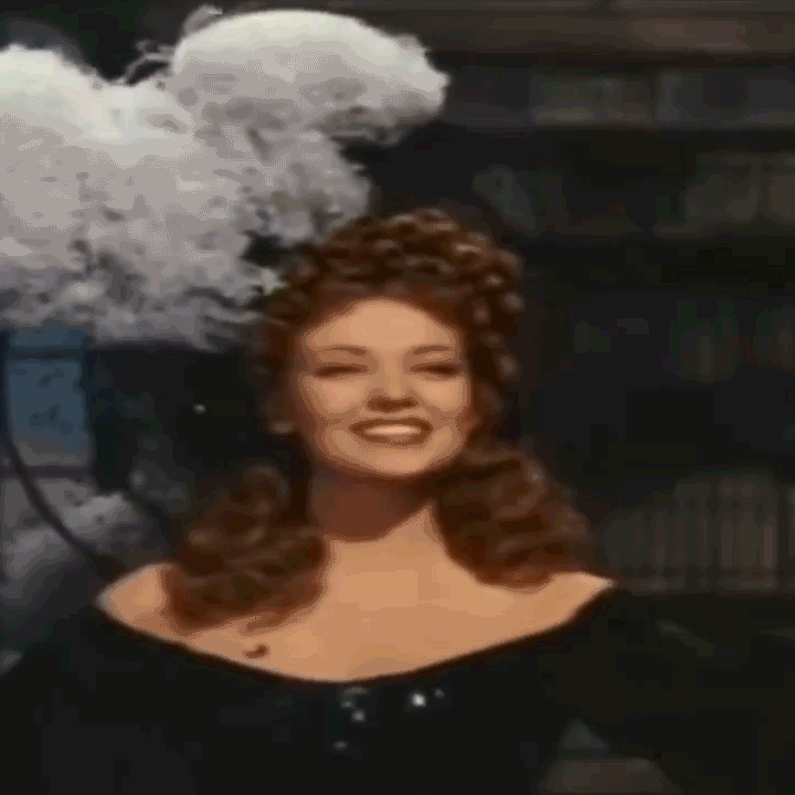 Linda Darnell as Amber St Clare, star of 1947 film Forever Amber. She bows in an enormous feathered head-dress, smiling cheekily