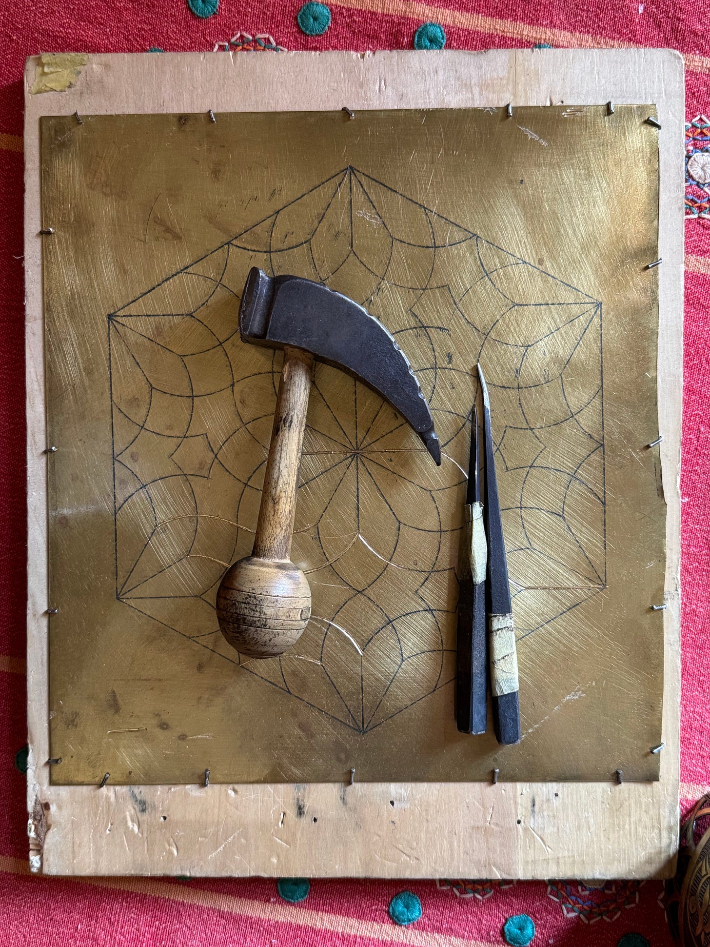Traditional brassworking tools resting on a brass sheet etched with a geometric pattern.