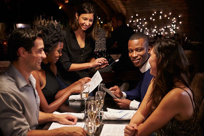A server smiles as she takes the order of four hip 20-somethings in a booth.