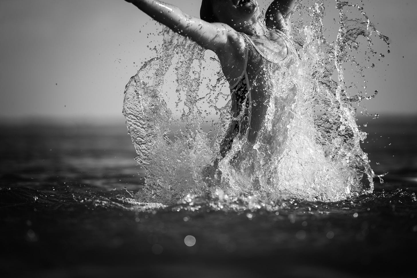 A swimmer rising from the water with arms spread wide and water falling from their arms into the lake.