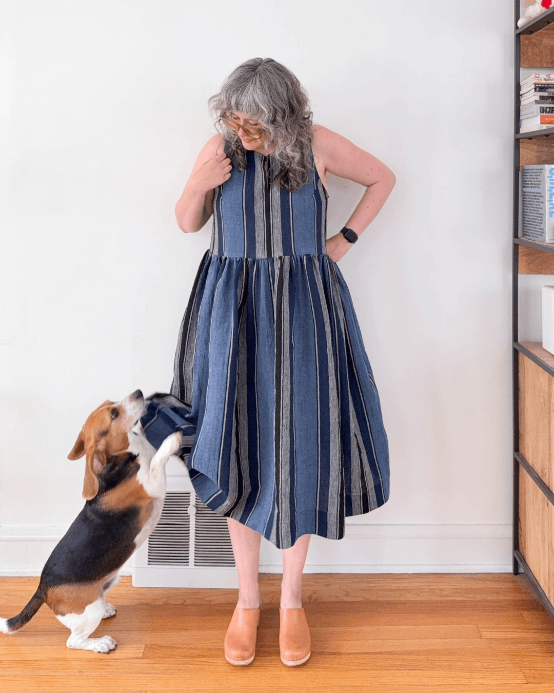 Woman wearing blue striped linen Austin Dress View B without button bands with tan clogs while beagle looks up at skirt