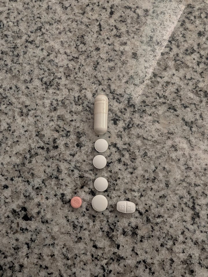 Pills on a granite countertop, arranged like a raised middle finger. A float pod in a room with a white bathmat. The pod lid is open, exposing blue water.
