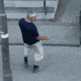 a man in a blue shirt and white shorts is staggering drunkenly down a street .