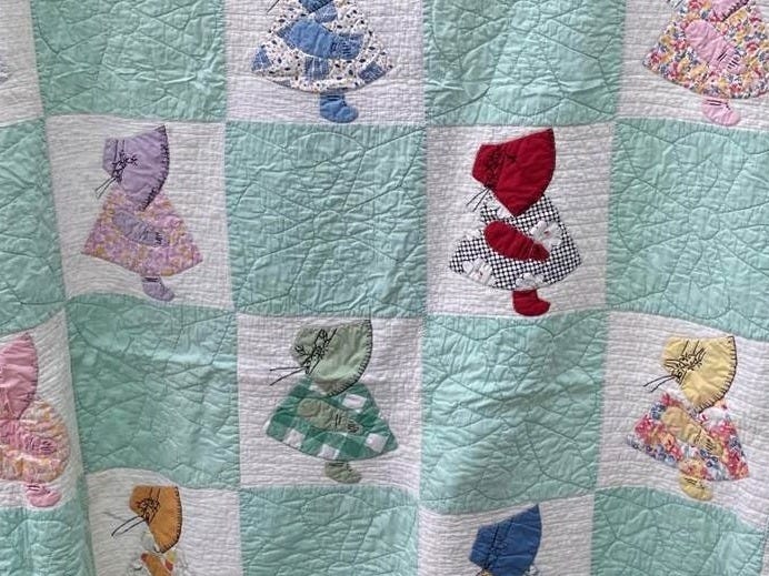 Part of a handmade quilt featuring seafoam squares alternating with white squares on which are appliqued pieces of various colors of fabric forming the profile of a little girl. 