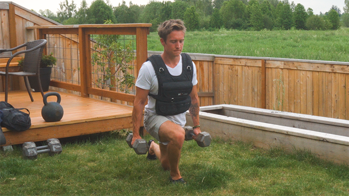 walking lunge wearing a weighted vest and holding a dumbbell in each hand