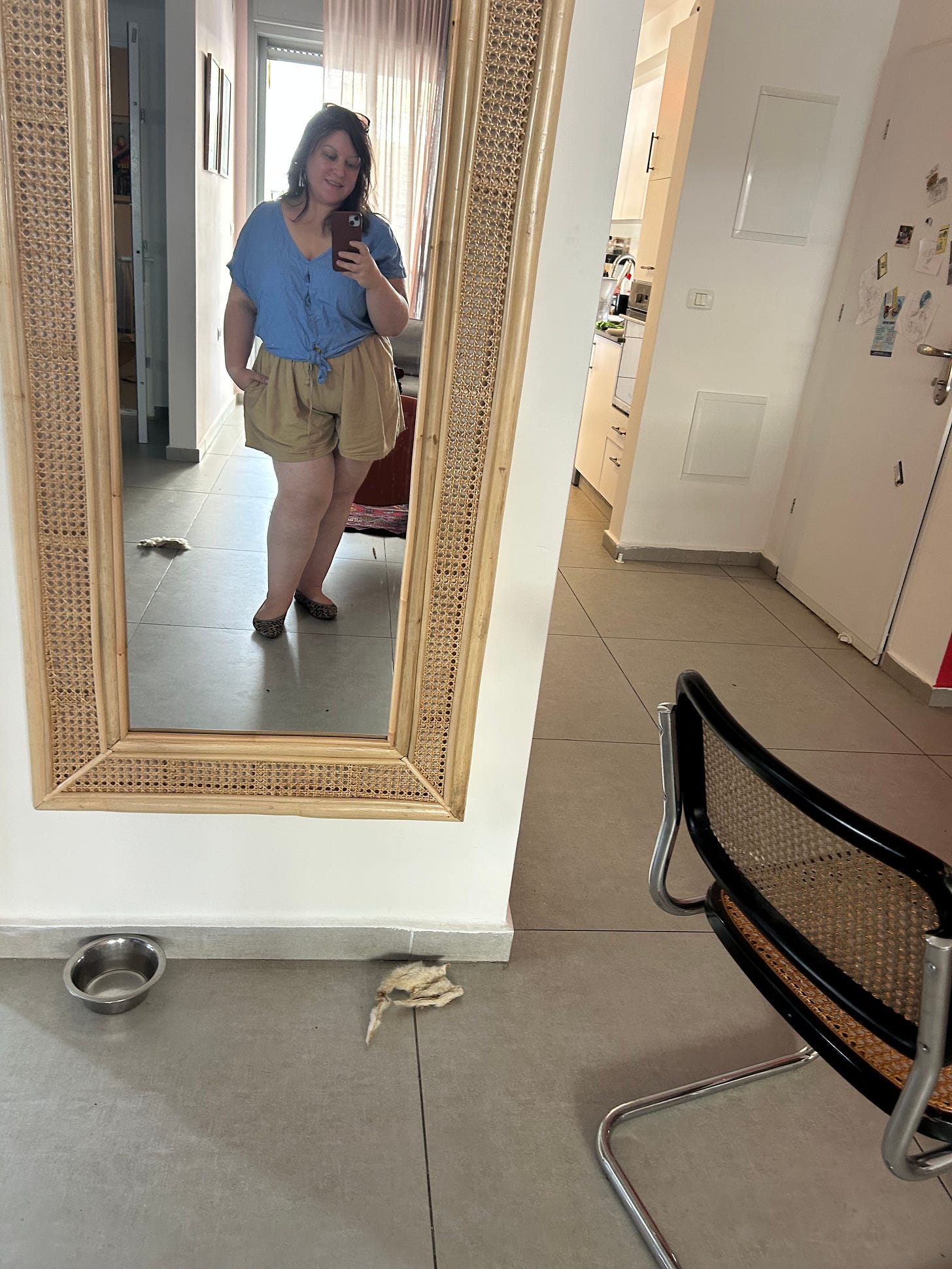 chedva ludmir kleinhandler taking a mirror selfie in a light blue linen shirt and tan shorts