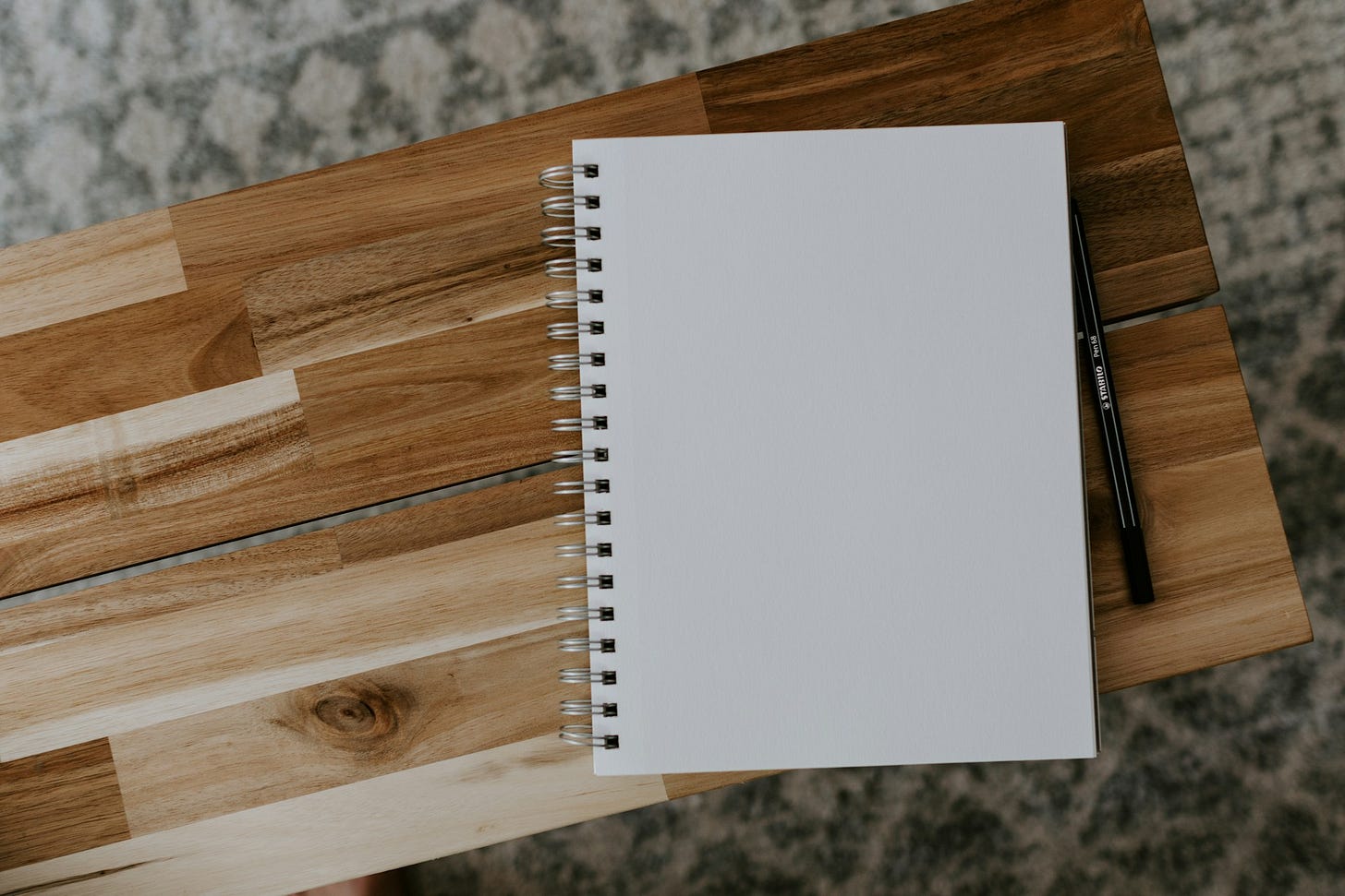 A spiral notebook and black pen on a wooden table