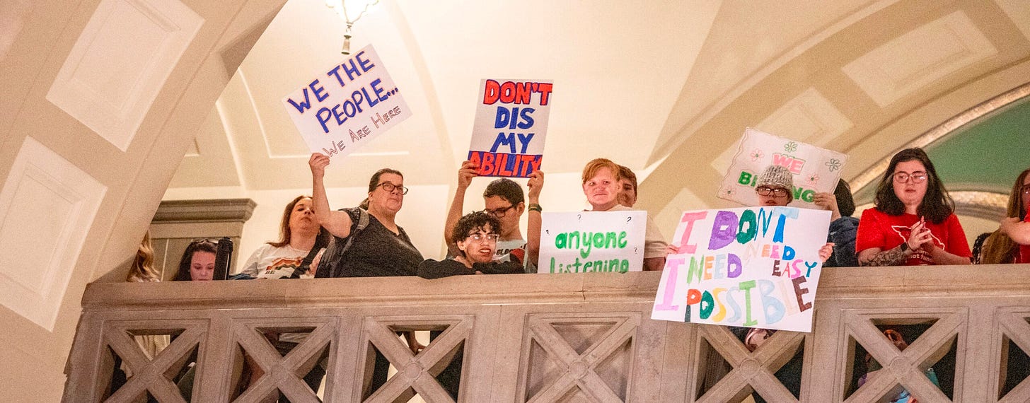 Disabled protestors hold signs inside the Missouri capitol. They are on a balcony holding signs. Don’t dis my ability. Anyone listening? I don’t need easy, I need possible. Disabled protestors hold signs inside the Missouri capitol. They are on a balcony holding signs. Don’t dis my ability. Anyone listening? I don’t need easy, I need possible.