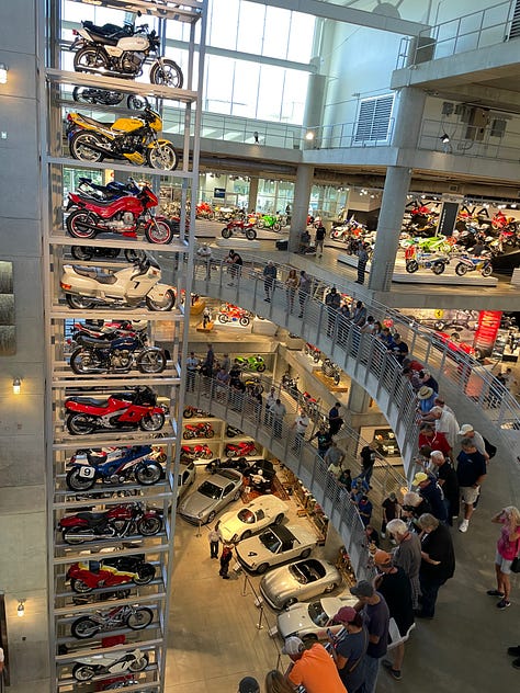 Barber Vintage Motorsports Museum Sign; vintage motorcycles on display; Jessica with her hair in two braids in one of the areas of the bike museum;dozens of bikes stacked on a very tall display; King Kenny Roberts wearing a cowboy hat and sitting on a yellow bike