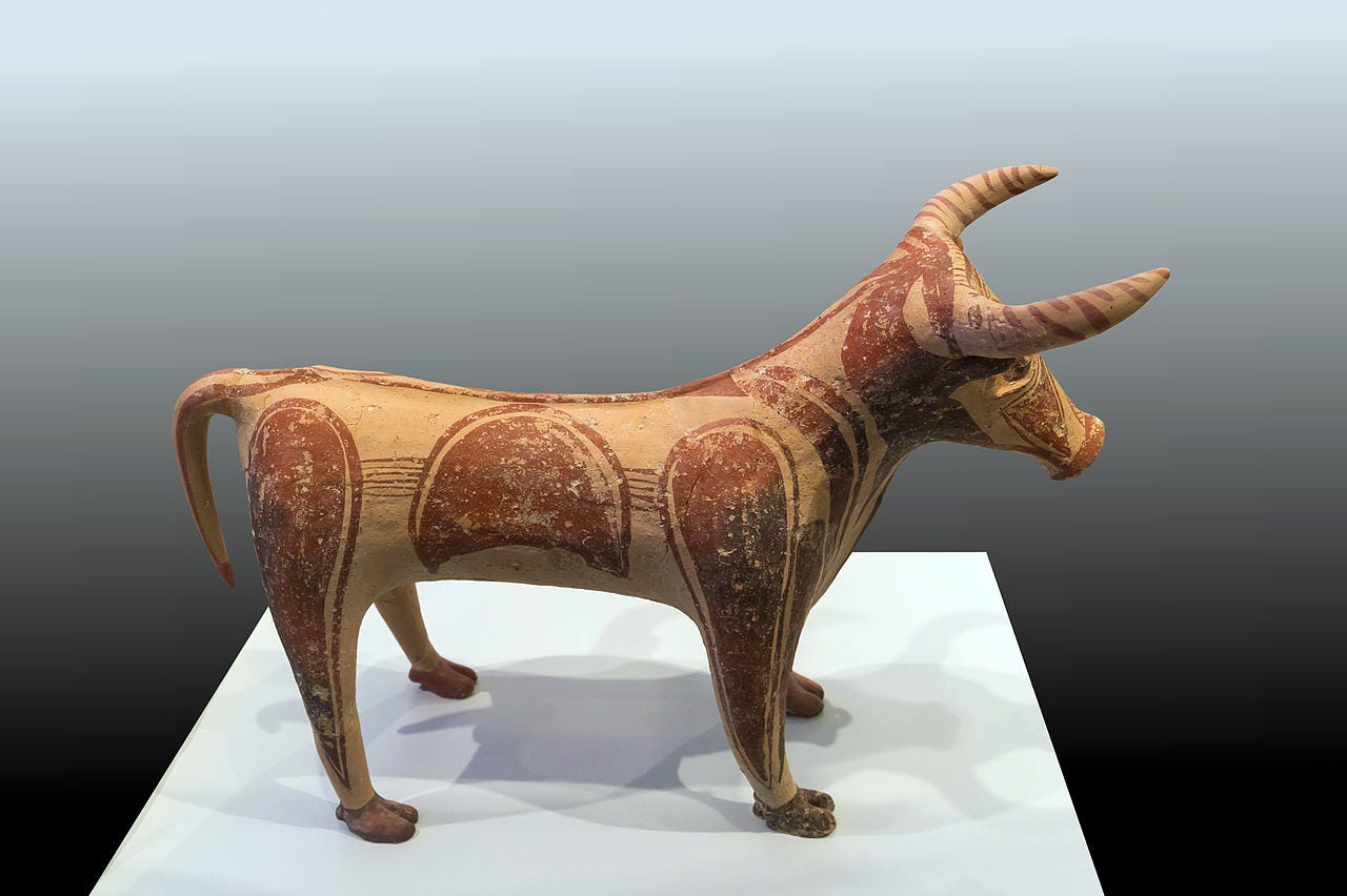 Ceramic figurine of a horned cow or bull. It is standing, facing right, and has large reddish spots painted all over its tan body.
