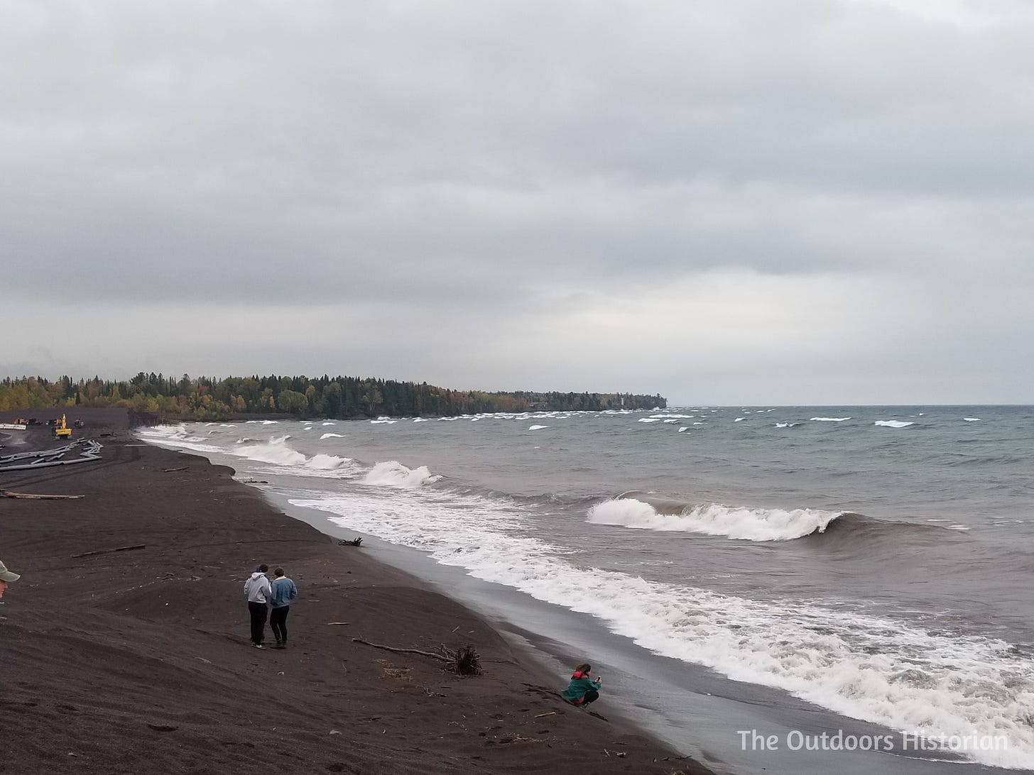Students stand on the shoreline. What used to be an eroding bluff, has been regraded to a gentle slope. An excavator sits in the distance.