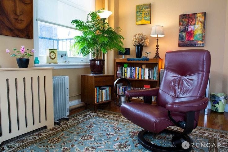This may contain: a living room with a radiator, bookshelf and chair in it