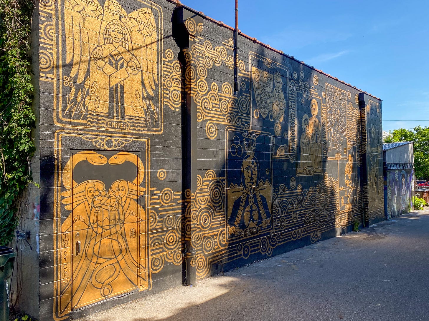 A mural of gold linework on a black wall depicting tarot-inspired imagery, including an angel figure labeled 'Empress' and geometric patterns.