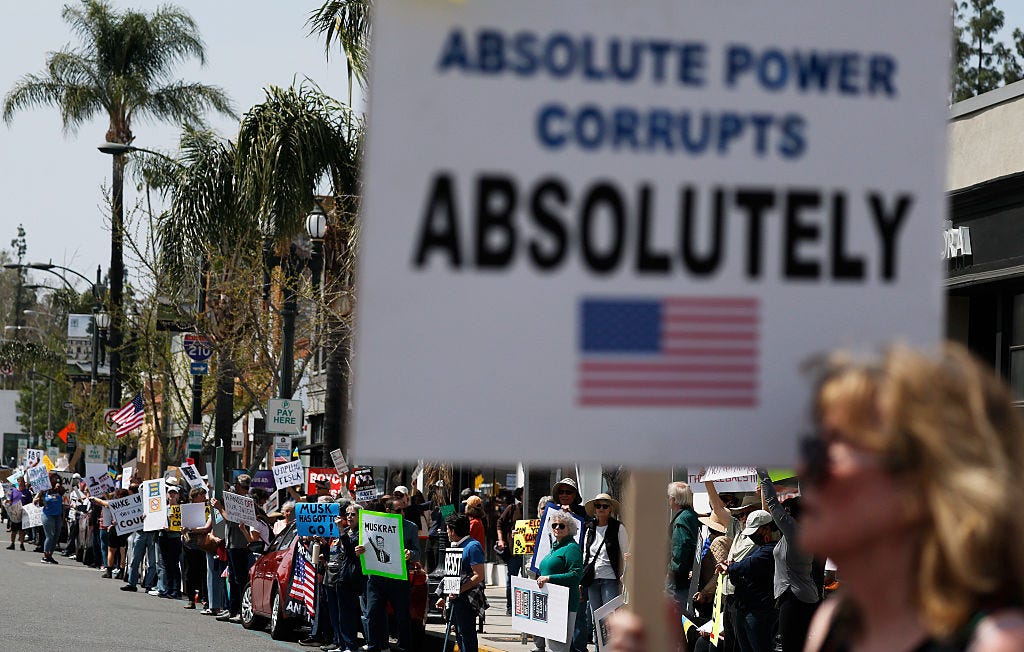 Image of a crowd of protestors on a Los Angeles area street; in the foreground a sign is visible, reading "Absolute Power Corrupts Absolutely"