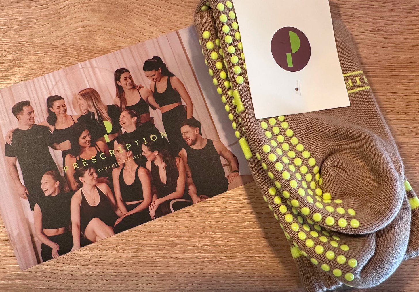 Prescription Pilates studio postcard of the instructor team in black, next to a pair of taupe grip socks with lime green dots Prescription Pilates studio postcard of the instructor team in black, next to a pair of taupe grip socks with lime green dots