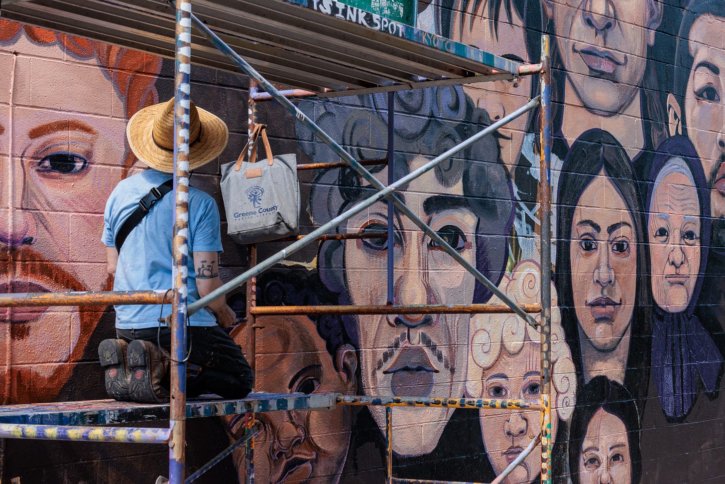 Pierre Nagley works on scaffolding, framed by the crisscrossing metal bars, painting one of the mural's portrait faces.