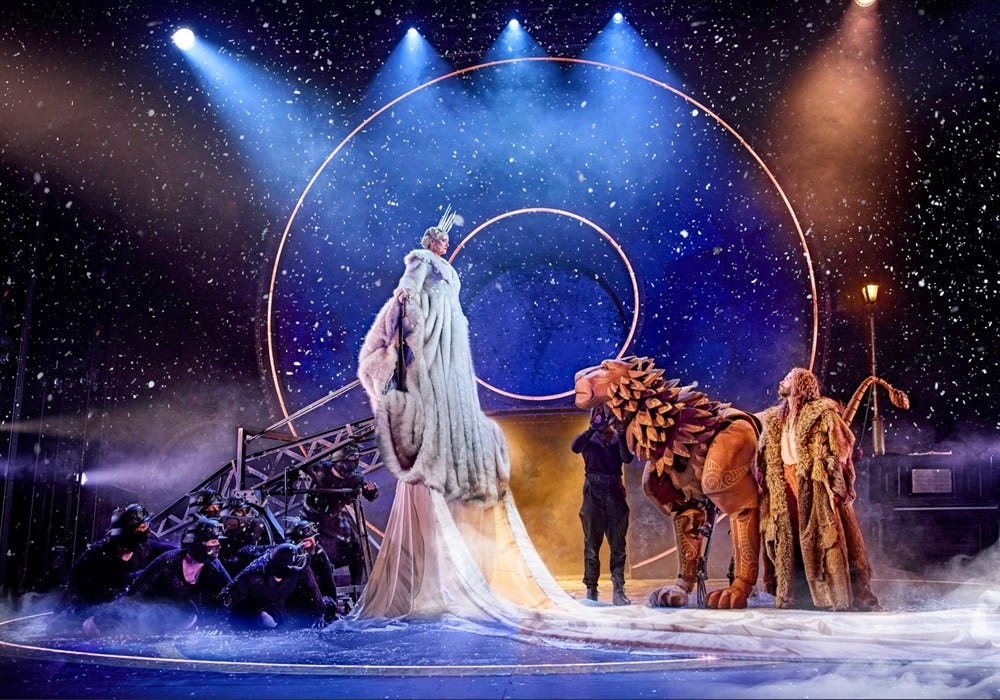 scene from the stage production of the lion the witch and the wardrobe with the white witch elevated next to the wooden lion with a starry background