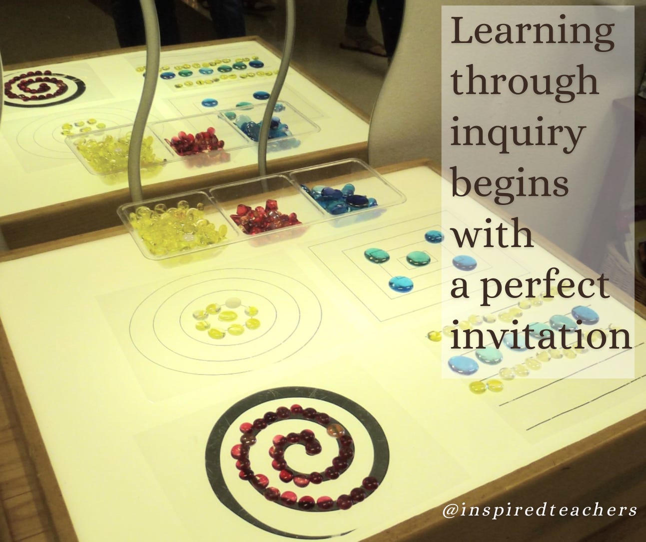 A light table has geometric shapes and glass beads.  there is a mirror above the table reflecting the light.