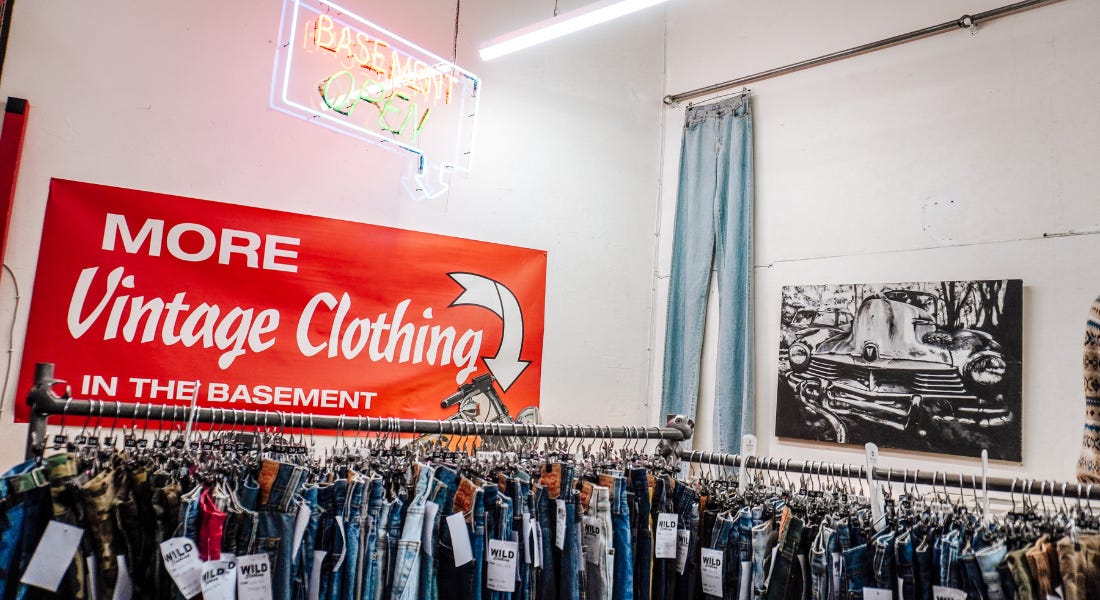 A vintage shop interior with jeans on rails, a red vintage sign, and a long pair of jeans on the wall